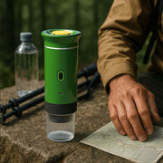 NØMA portable espresso maker in green on hiking trail with map, trekking poles and water bottle.
